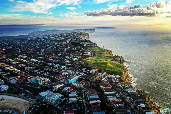Aerial view of a coastal Australian neighborhood with houses near the ocean, highlighting a popular area for real estate investment with scenic ocean views.​