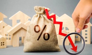 A burlap money bag with a percentage symbol, a red downward arrow, and wooden house models representing falling interest rates or declining property values.