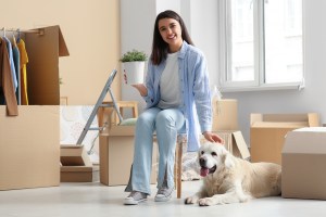 A happy woman sitting among moving boxes with her dog, settling into a new home.