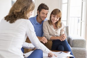 Happy couple meeting with a professional advisor, reviewing documents together at a table in a bright modern living room.
