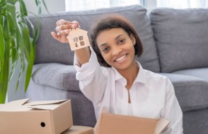 Young woman smiling while holding house keychain, surrounded by moving boxes