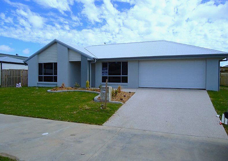 Modern single-story house with a manicured front lawn, concrete driveway, and a bright blue sky.