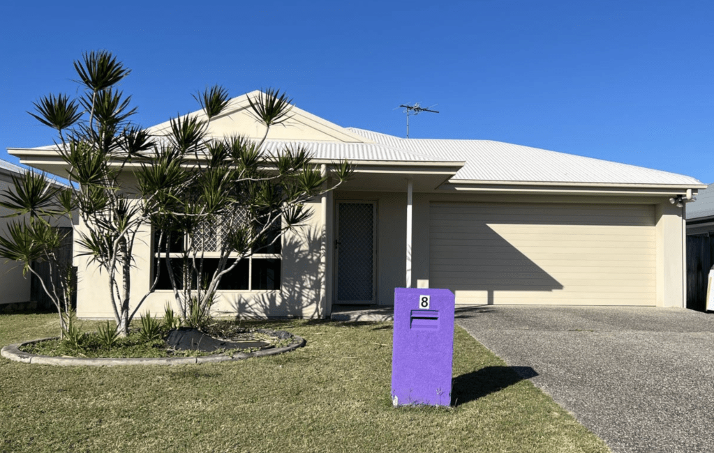 Modern single-storey home in Bucasia, QLD with a white roof, double garage, tropical landscaping and a purple letterbox, set on a flat coastal block.
